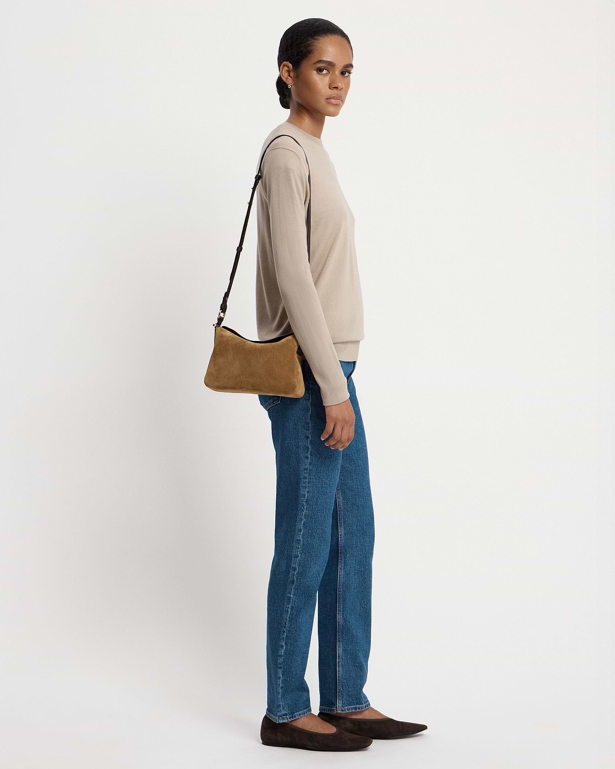 Woman wearing toffee suede shoulder bag with espresso strap, beige top and jeans.