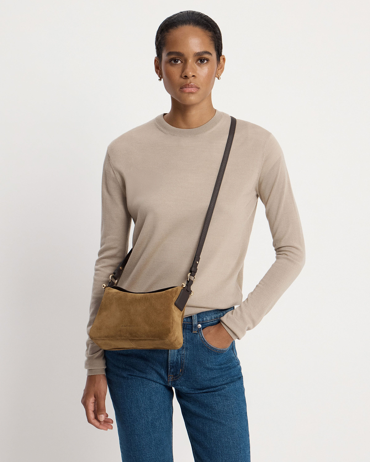 Model wearing Strathberry Sway toffee suede crossbody bag with espresso strap over shoulder.
