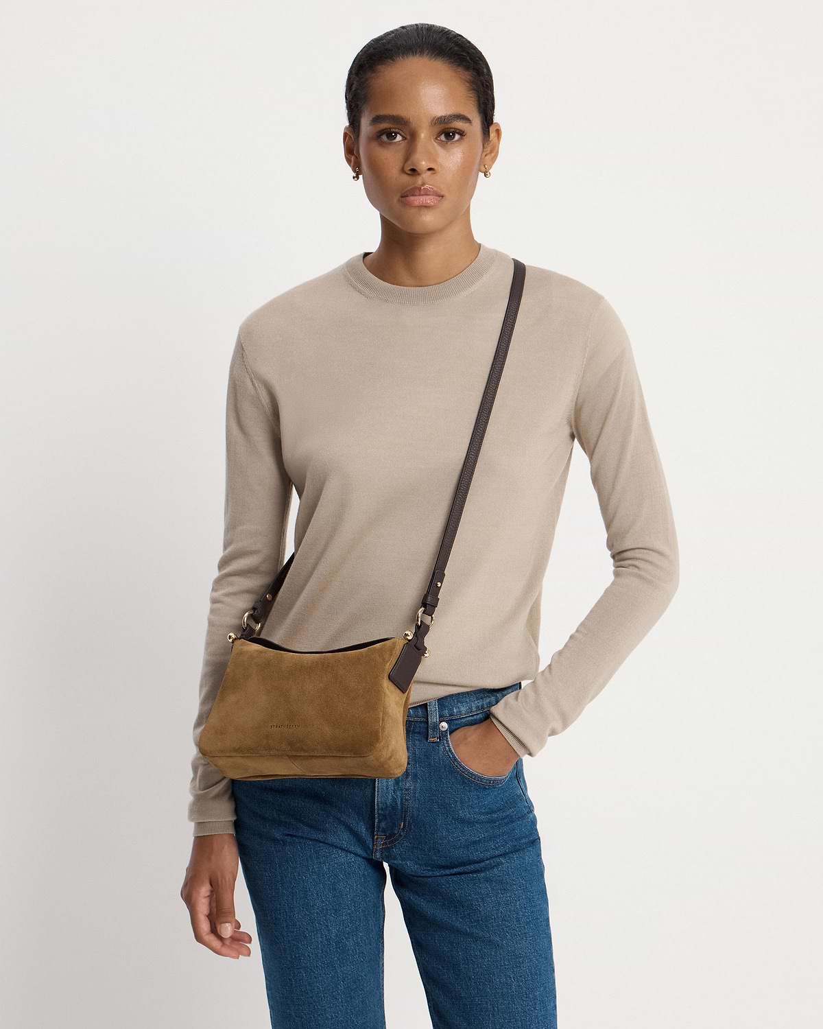 Model wearing Strathberry Sway toffee suede crossbody bag with espresso strap over shoulder.