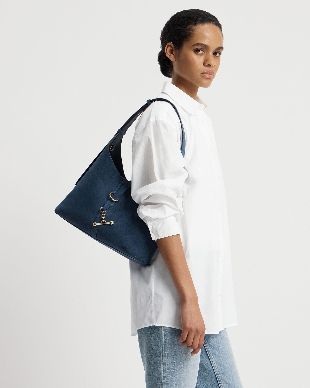 Model wearing a white shirt carries a loch blue suede Kite Hobo shoulder bag.