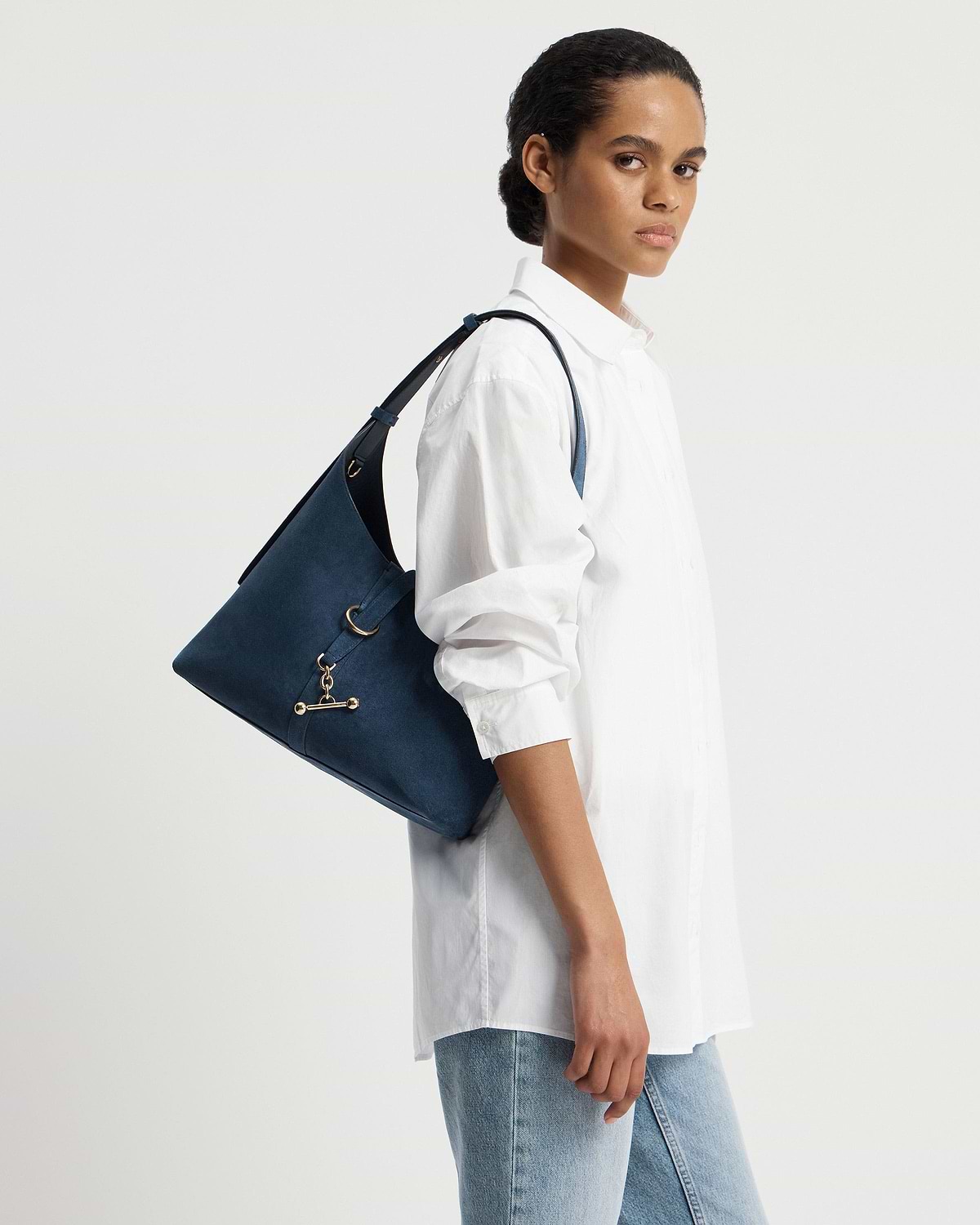 Model wearing a white shirt carries a loch blue suede Kite Hobo shoulder bag.