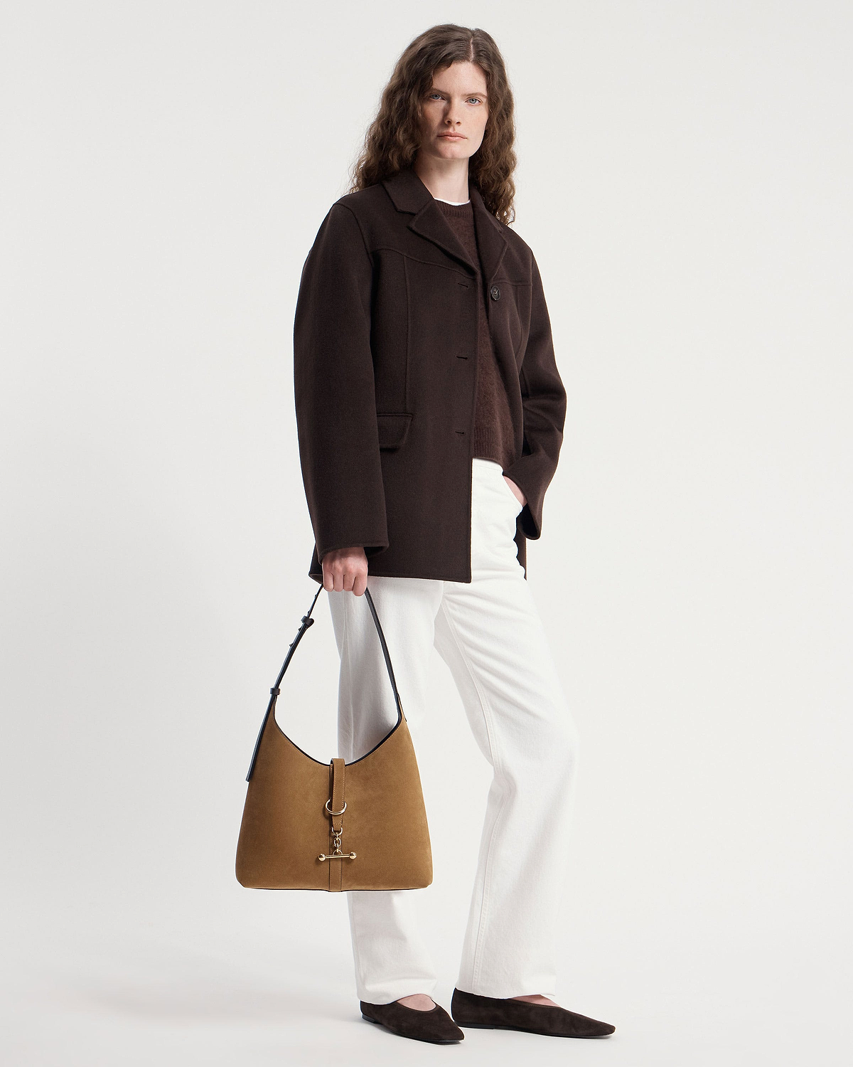 Model wearing brown coat, white trousers, holding toffee suede hobo bag with espresso strap.