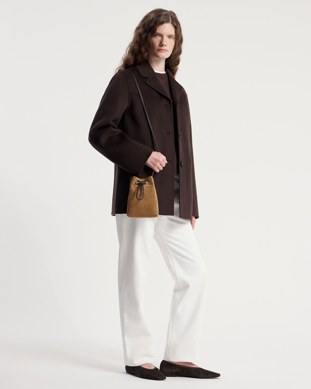 Model wearing a toffee suede drawstring midi pouch with espresso shoulder strap.