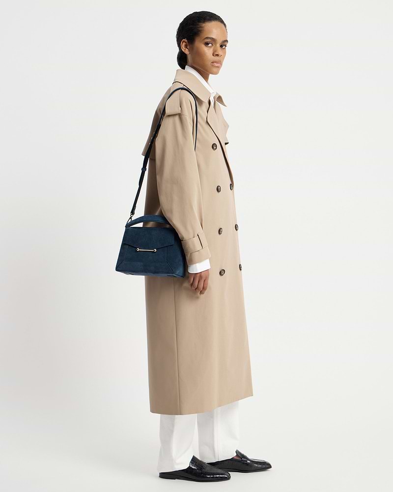 Model wearing beige trench coat carrying a loch blue suede mosaic bag.