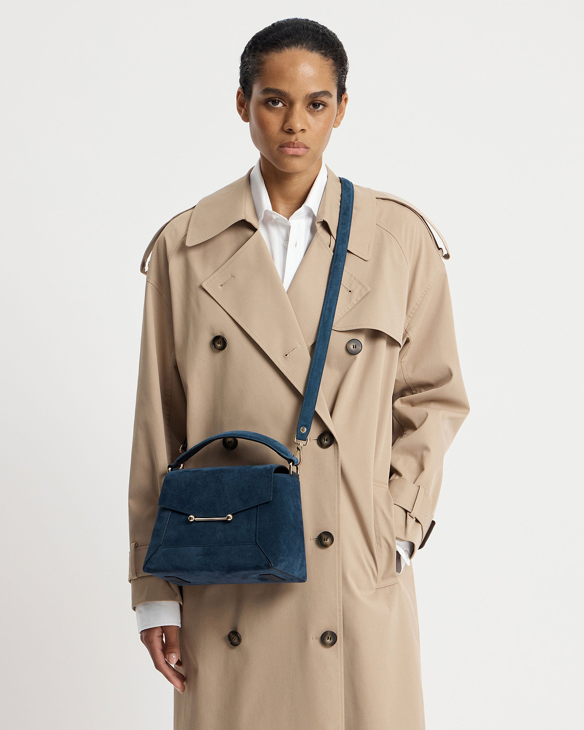 Model wearing beige trench coat with loch blue suede mosaic bag worn crossbody.