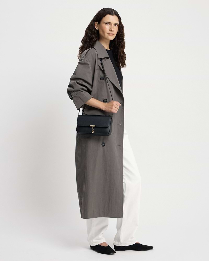 Woman wearing a trench coat carrying a black Nocturn clutch with gold clasp.
