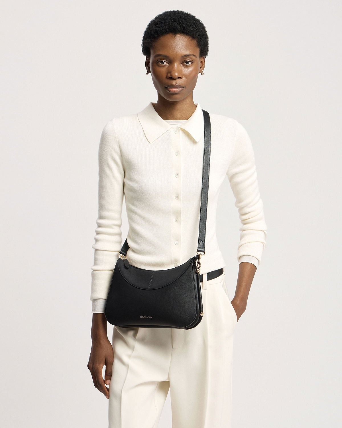 Model wearing cream top and trousers with black Strathberry Nest Shoulder bag.