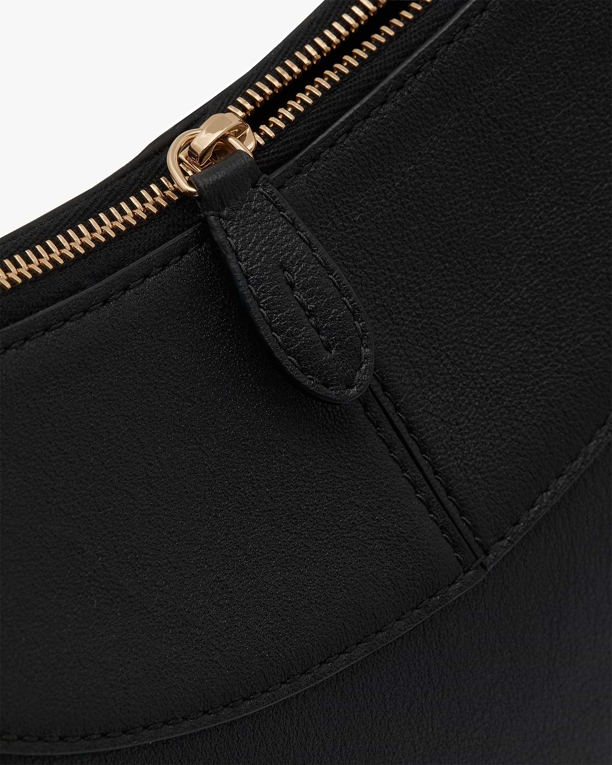 Close-up of black leather shoulder bag with gold zip pull and stitched seam.