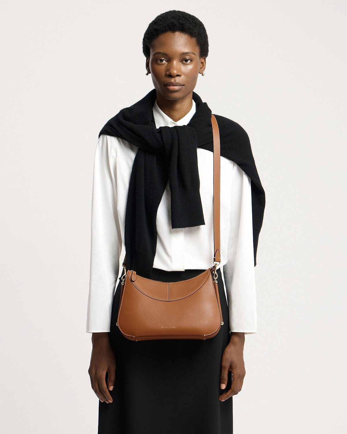 Model wearing tan Nest Shoulder bag worn crossbody over a white shirt.
