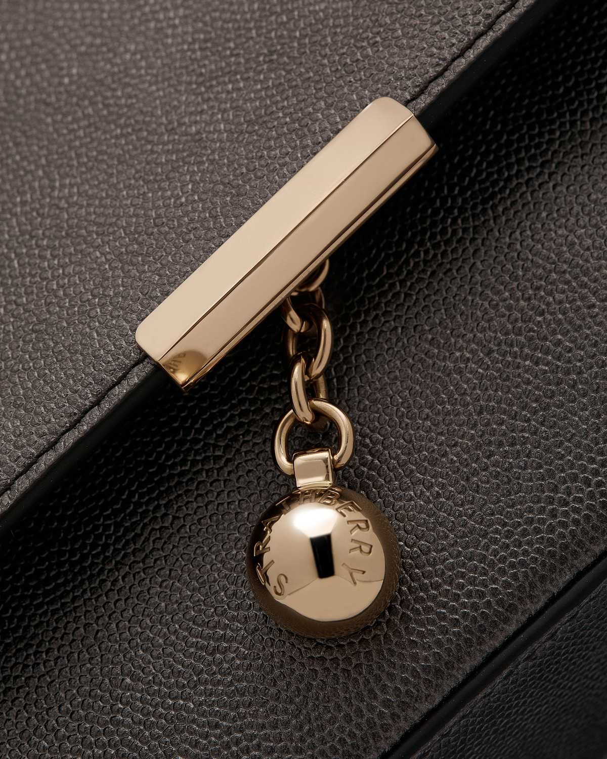 Close up of metallic anthracite caviar leather clutch showing gold bar clasp and Strathberry charm