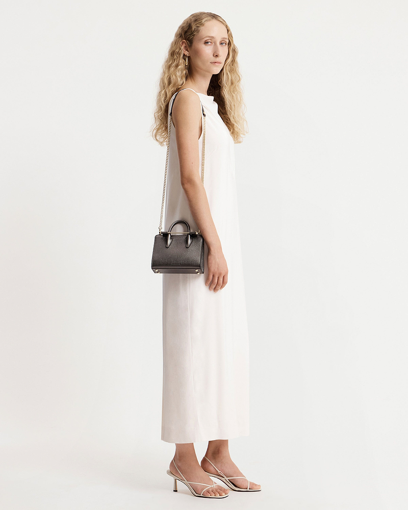 Model in white sleeveless dress holding a metallic anthracite nano tote with chain strap.