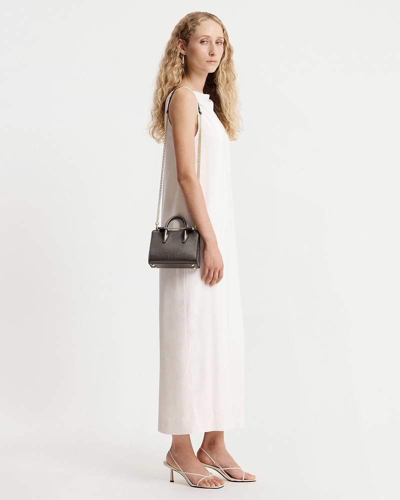 Model in white sleeveless dress holding a metallic anthracite nano tote with chain strap.