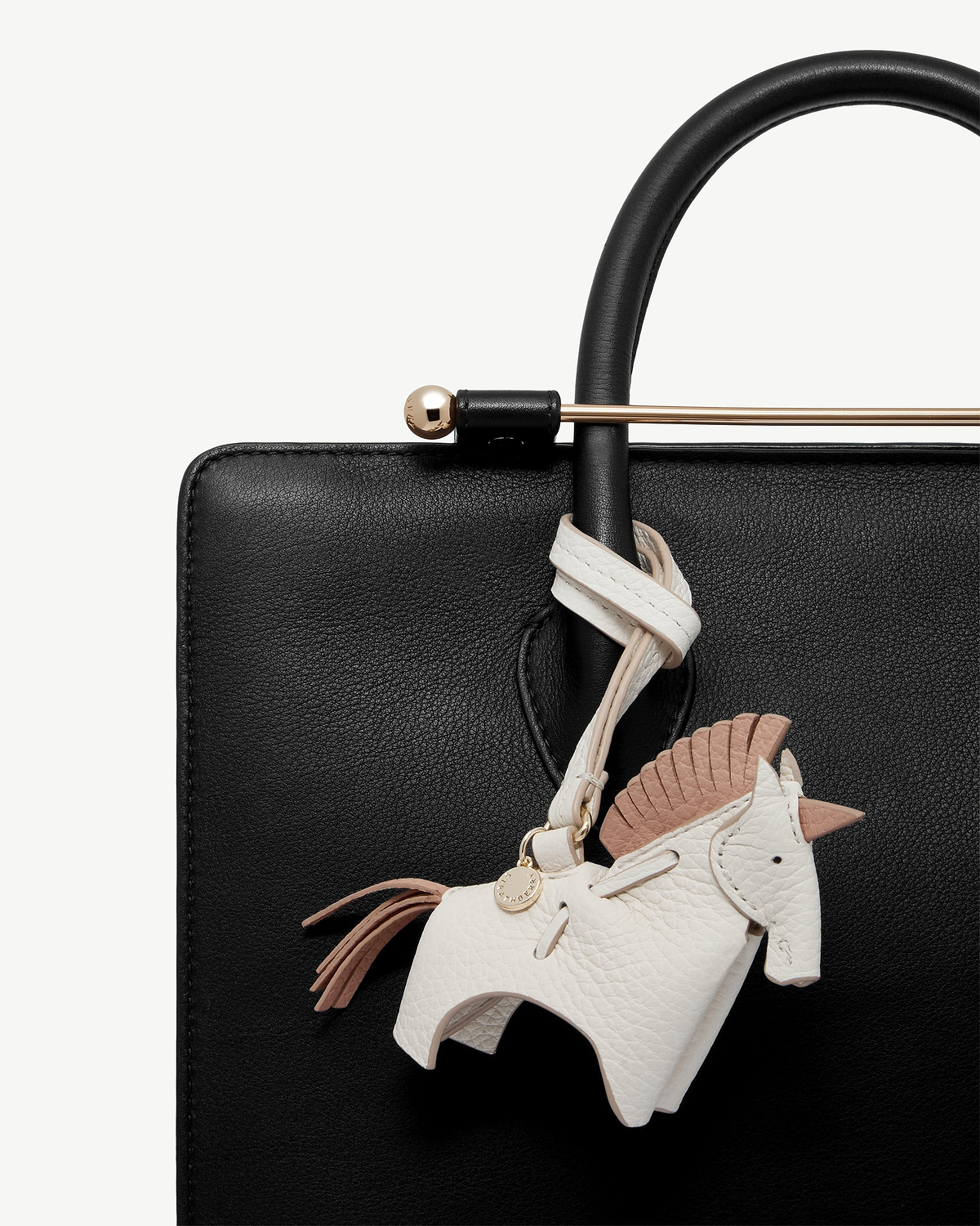 White peony unicorn leather bag charm hanging from black bag handle and gold bar.