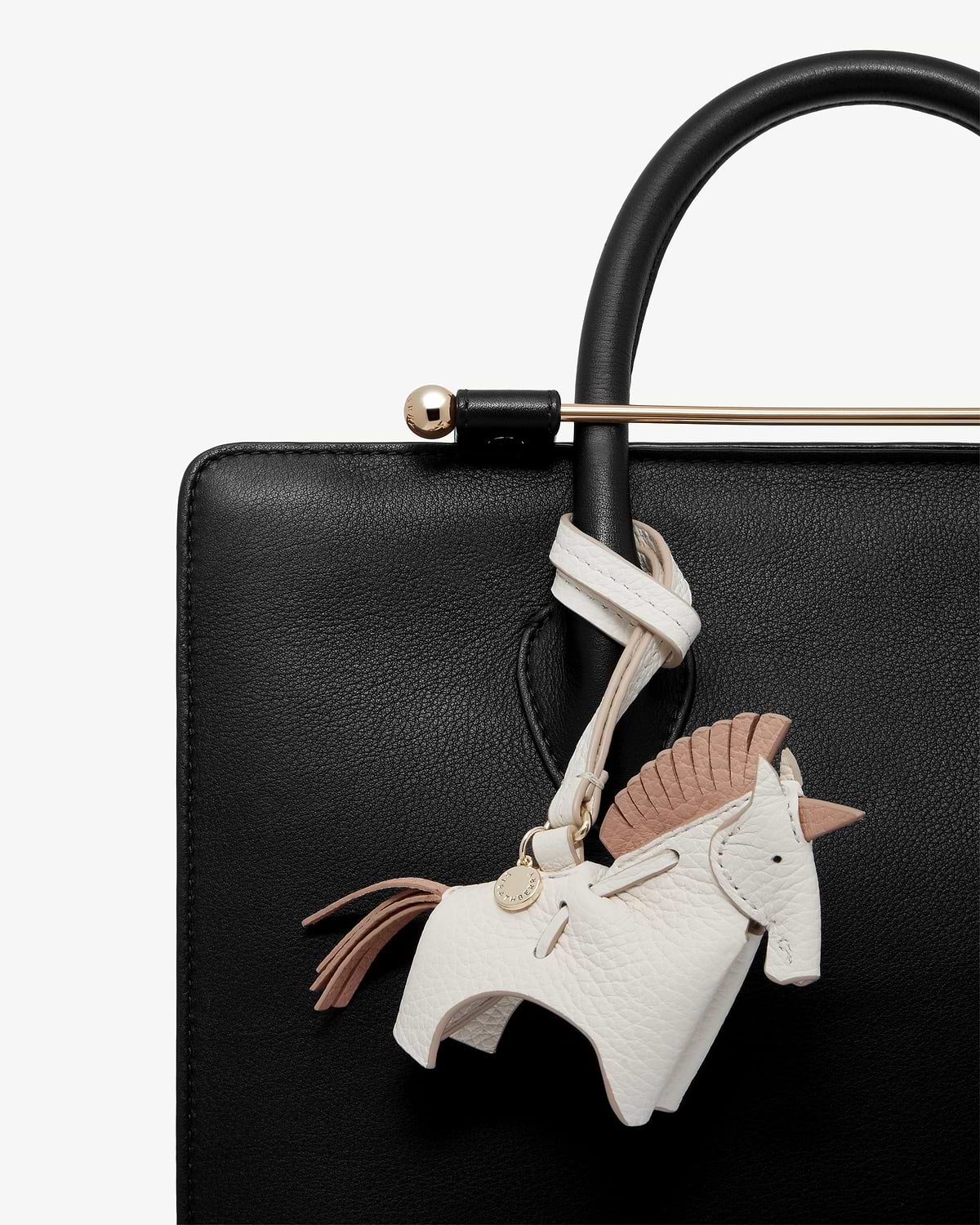 White peony unicorn leather bag charm hanging from black bag handle and gold bar.