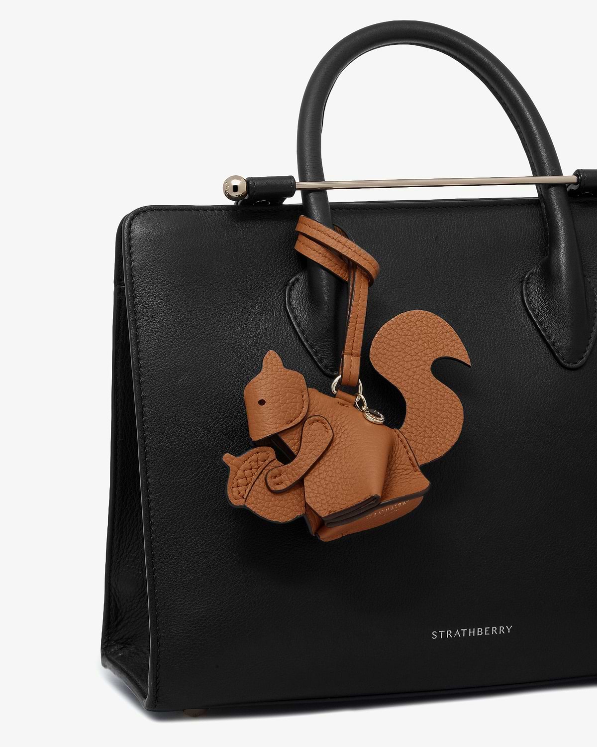 Tan squirrel leather bag charm hanging from black Strathberry tote handle.