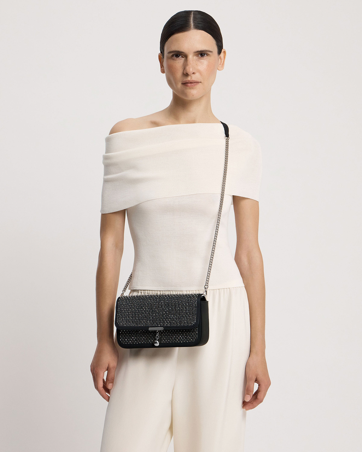 Model wearing black embroidered satin clutch with silver chain strap.