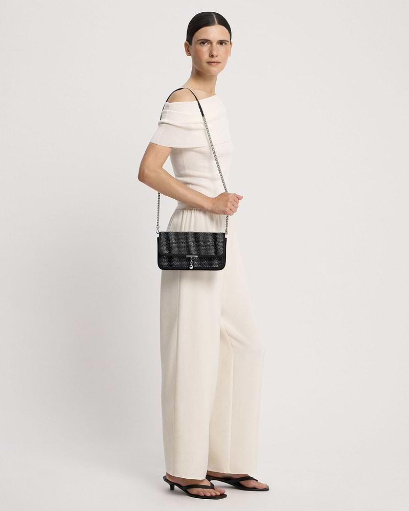 Model wearing a black embroidered satin clutch with a silver chain strap at hip.