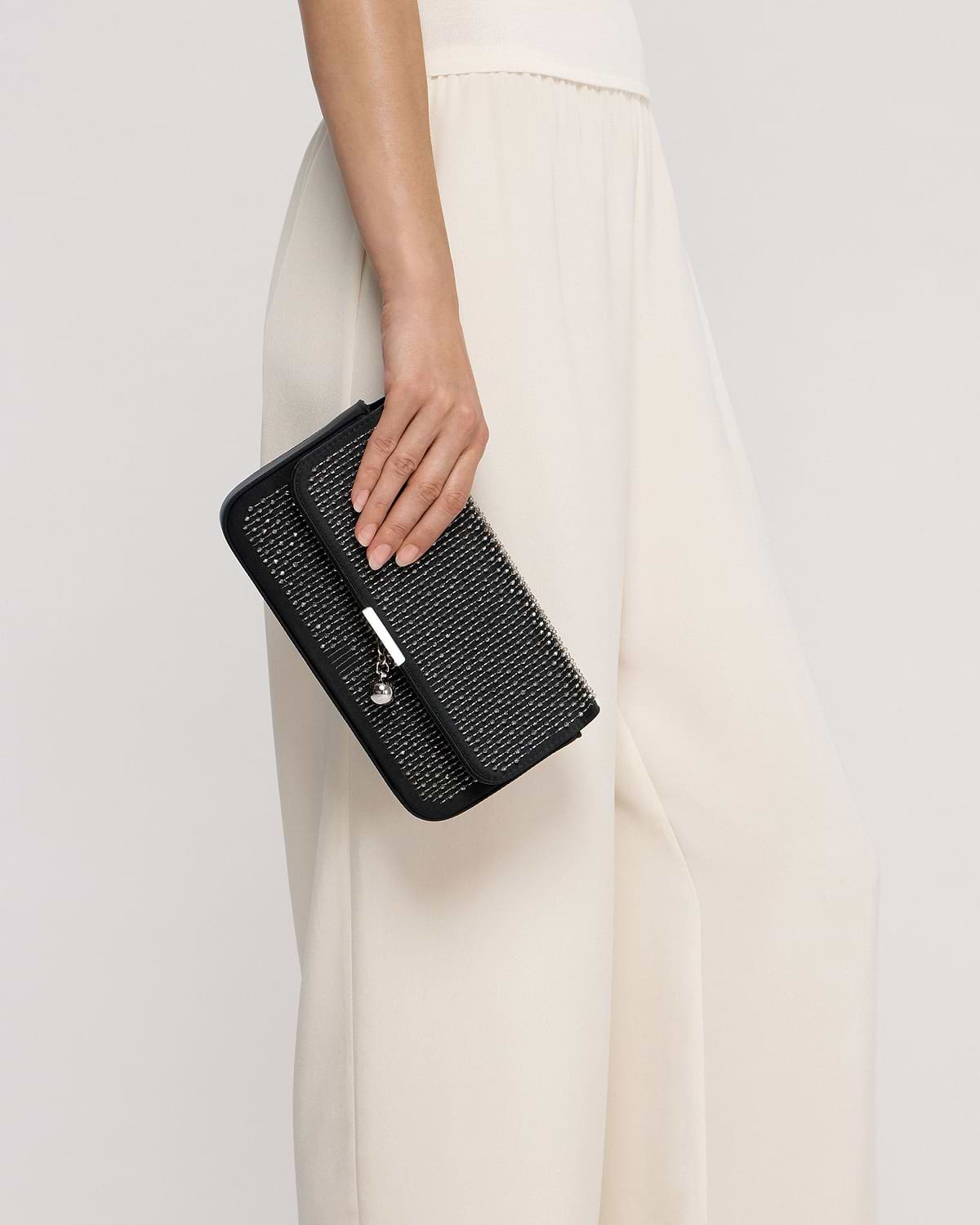 Hand holding black embroidered satin clutch against cream flowing skirt.