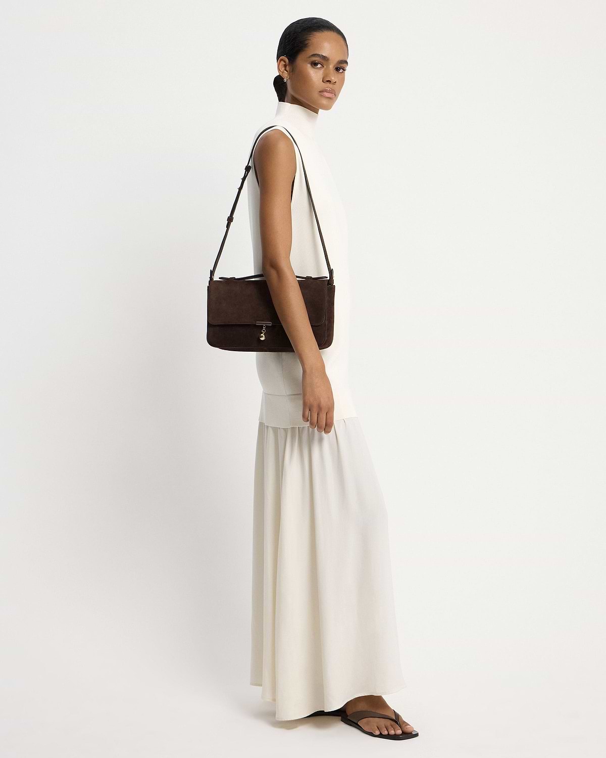 Model in white dress carrying espresso suede Nocturn Midi shoulder bag
