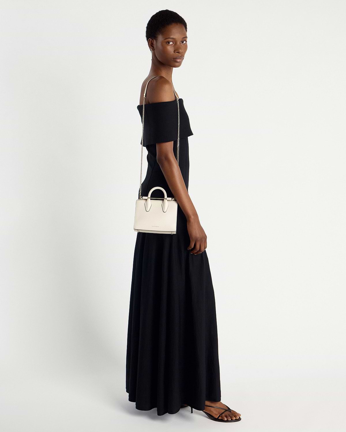 Model wearing black off-shoulder dress with vanilla nano tote on chain strap.