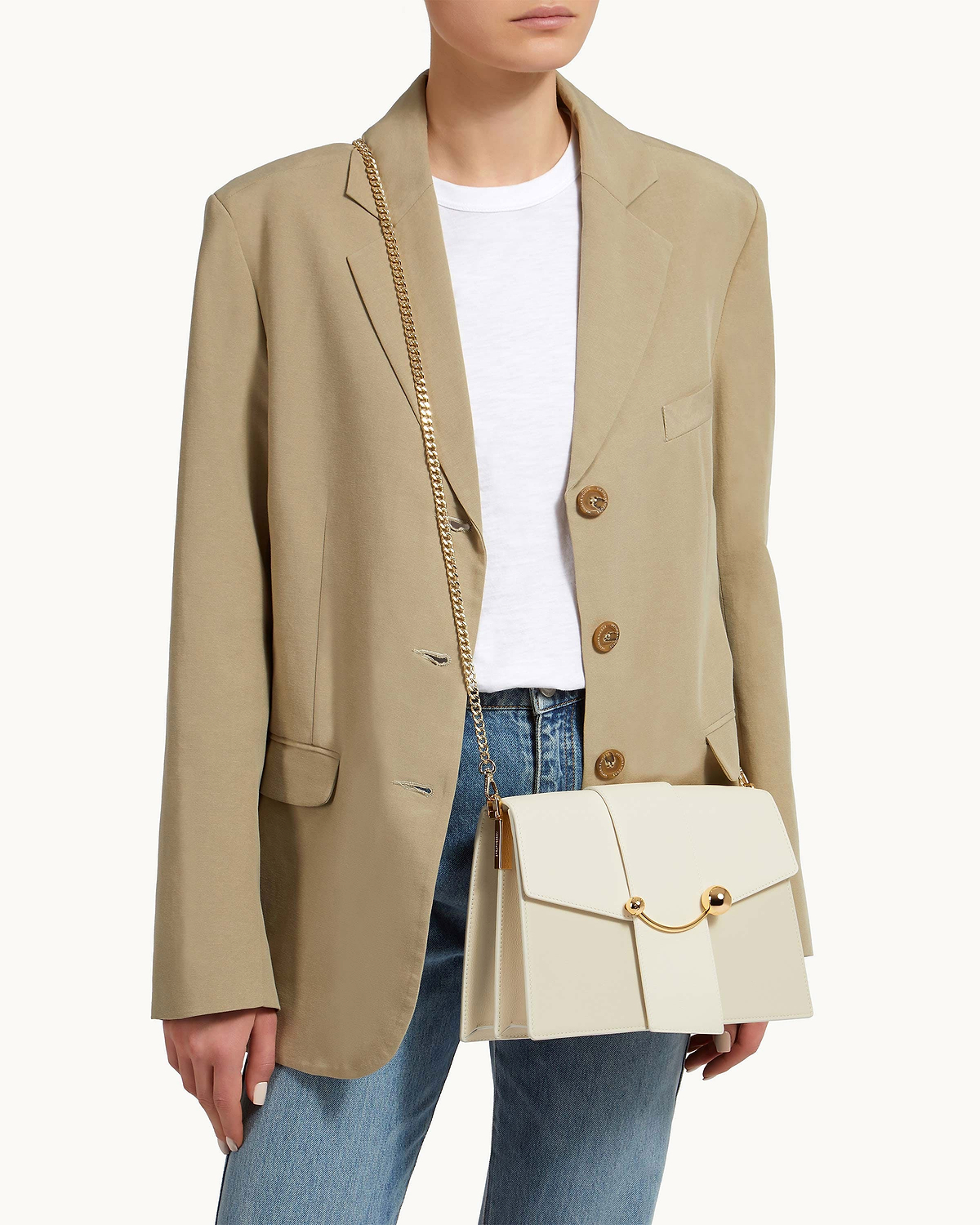 Model wearing beige blazer carrying cream bag on a gold short crossbody chain strap.