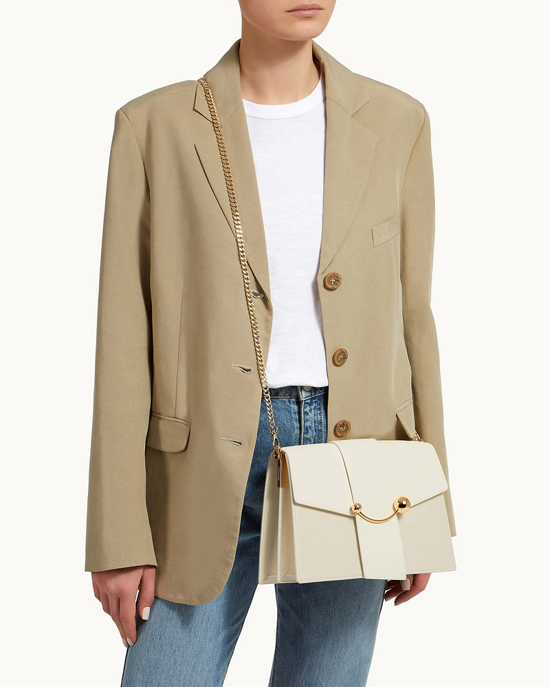 Model wearing beige blazer carrying cream bag on a gold short crossbody chain strap.