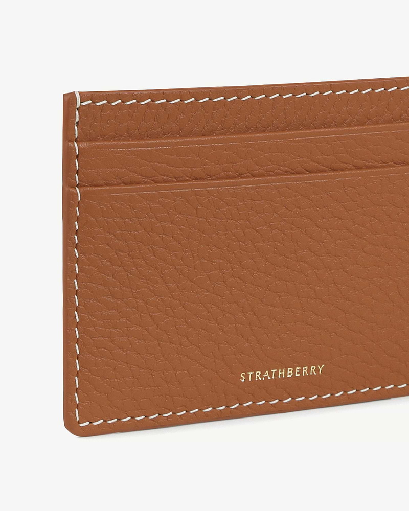 Tan leather cardholder corner with vanilla contrast stitching and gold Strathberry logo.