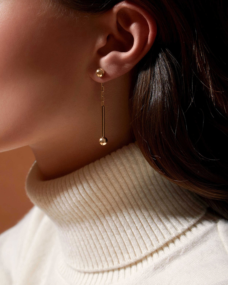 Ear wearing 22 carat gold gilded music bar drop earring with ball ends.