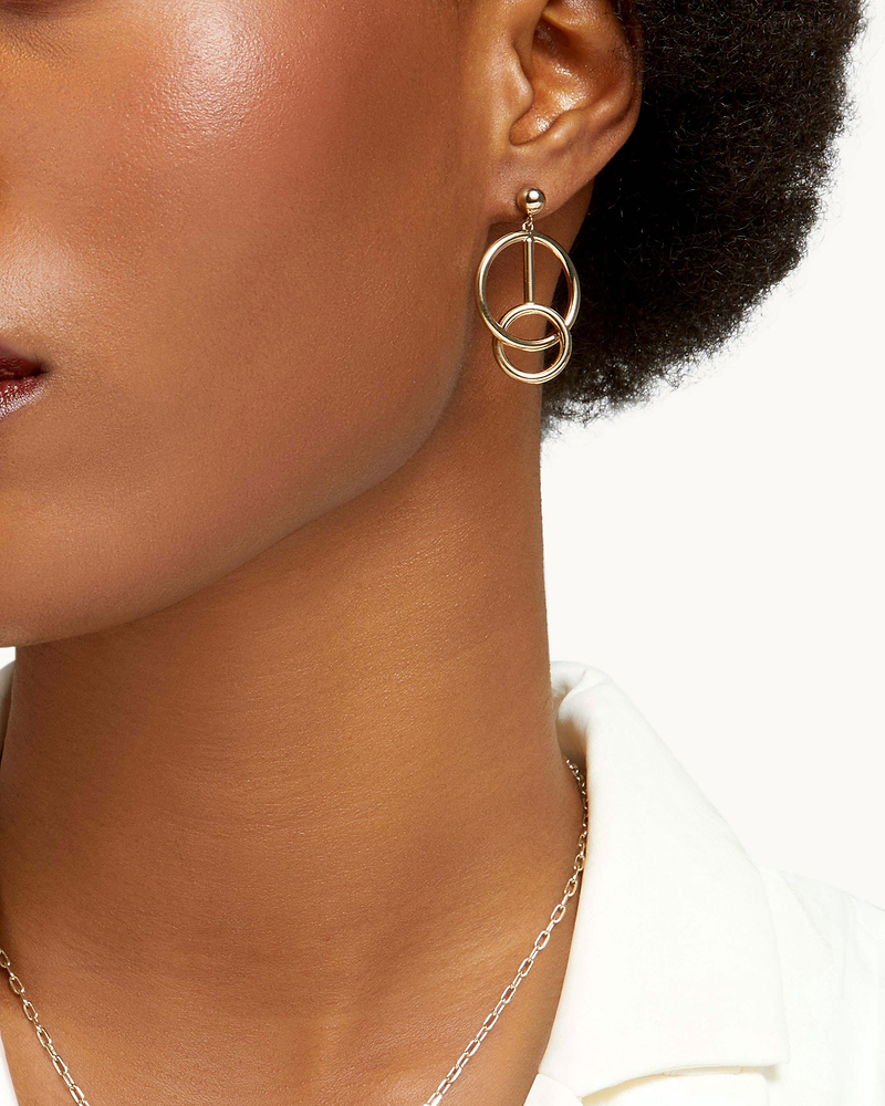 Ear wearing 22-carat gold-gilded music bar hoop earrings with interlocking rings.