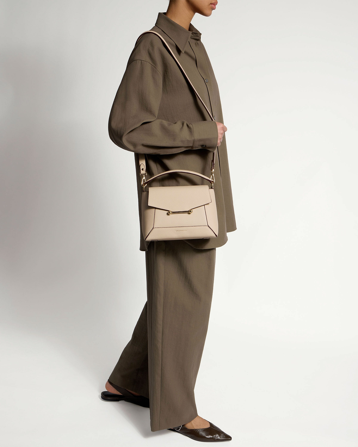 Model wearing oat-coloured mosaic bag across body with oversized brown shirt and wide trousers.