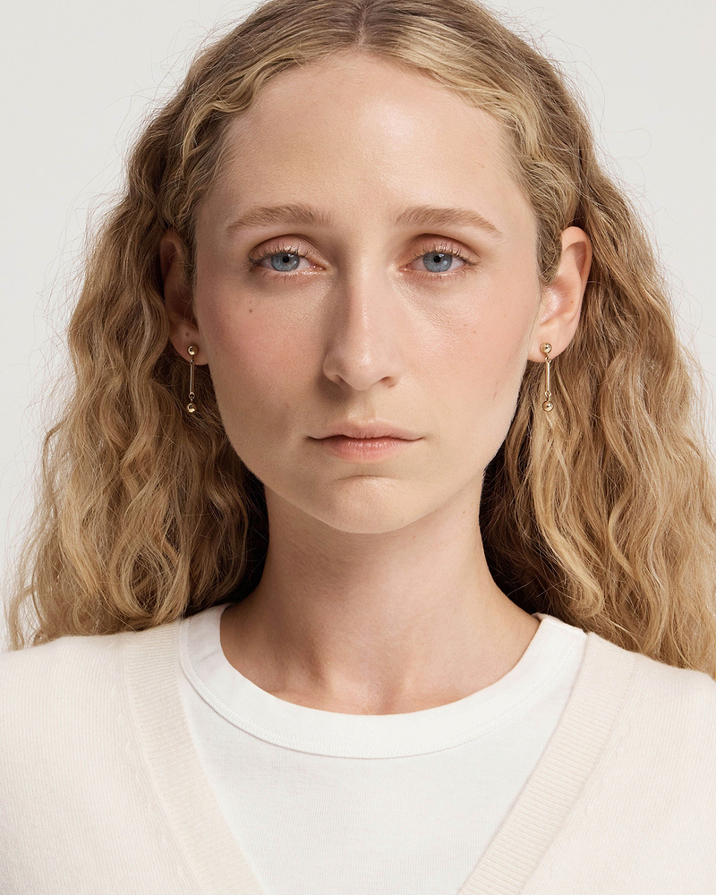 Woman wearing 22 carat gold-gilded music bar earrings, face and shoulders visible.