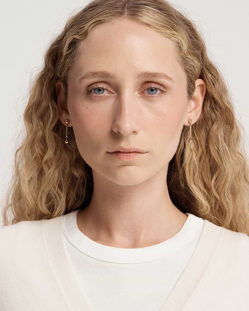 Woman wearing 22 carat gold-gilded music bar earrings, face and shoulders visible.