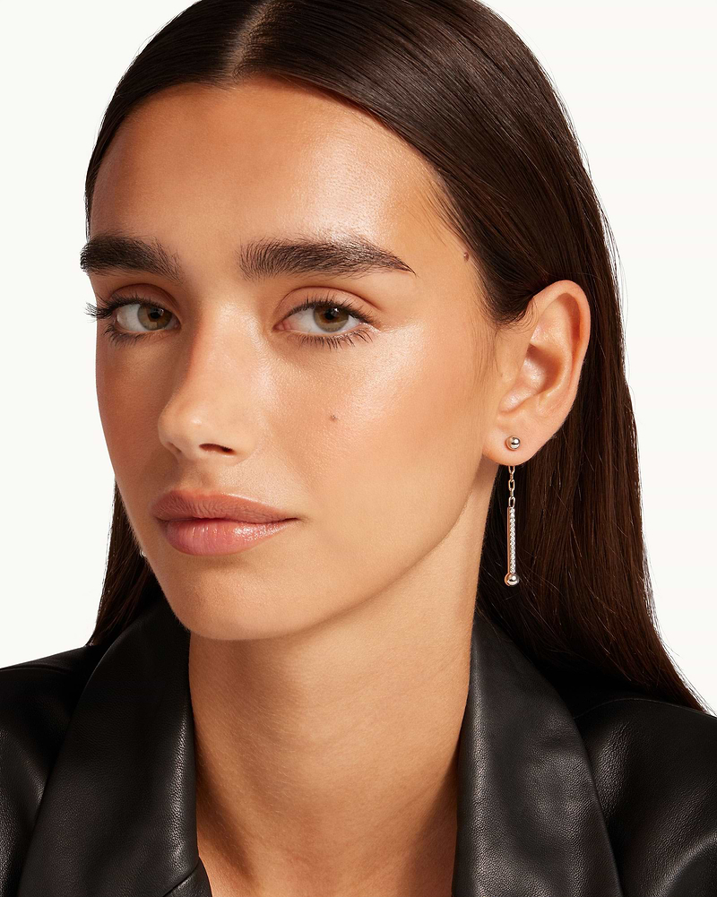 Model wearing silver crystal drop earrings with thin bar and small ball.