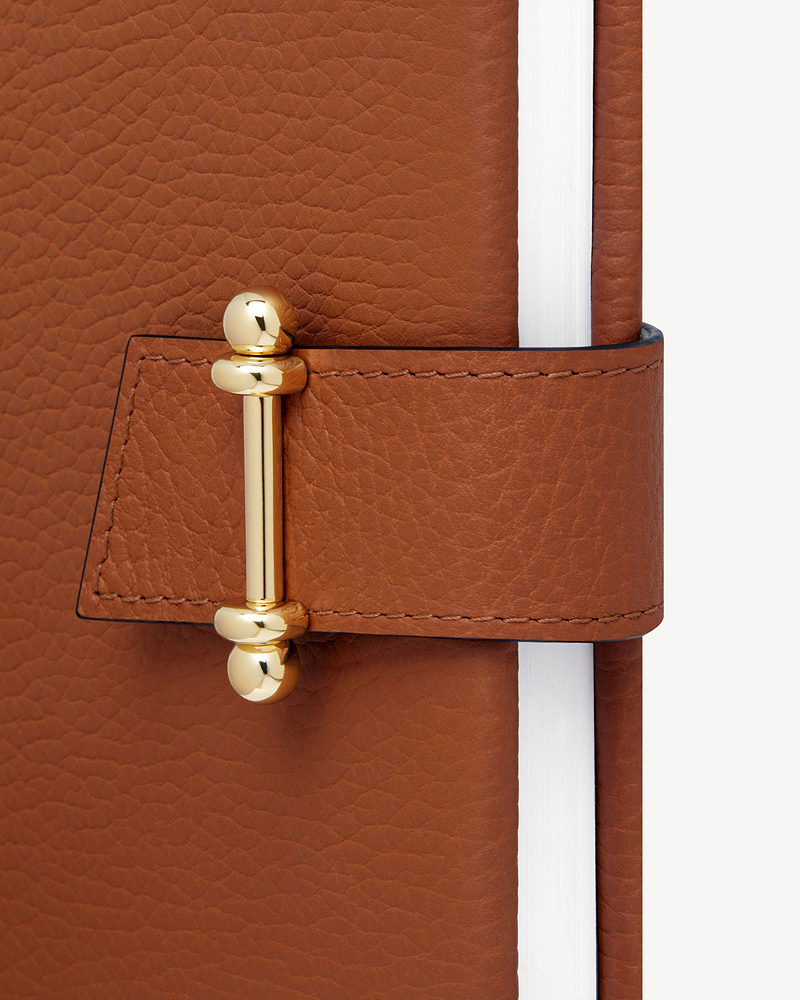 Tan leather notebook cover with gold bar closure and visible white page edges.