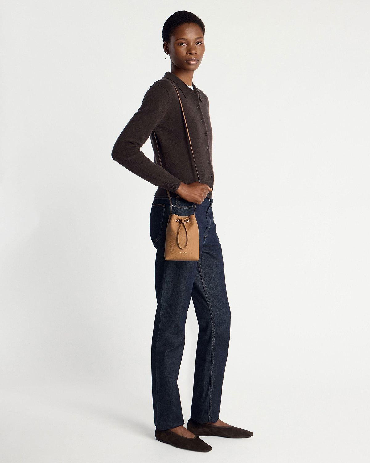 Model wearing caramel midi pouch crossbody with dark cardigan, jeans, brown flats.
