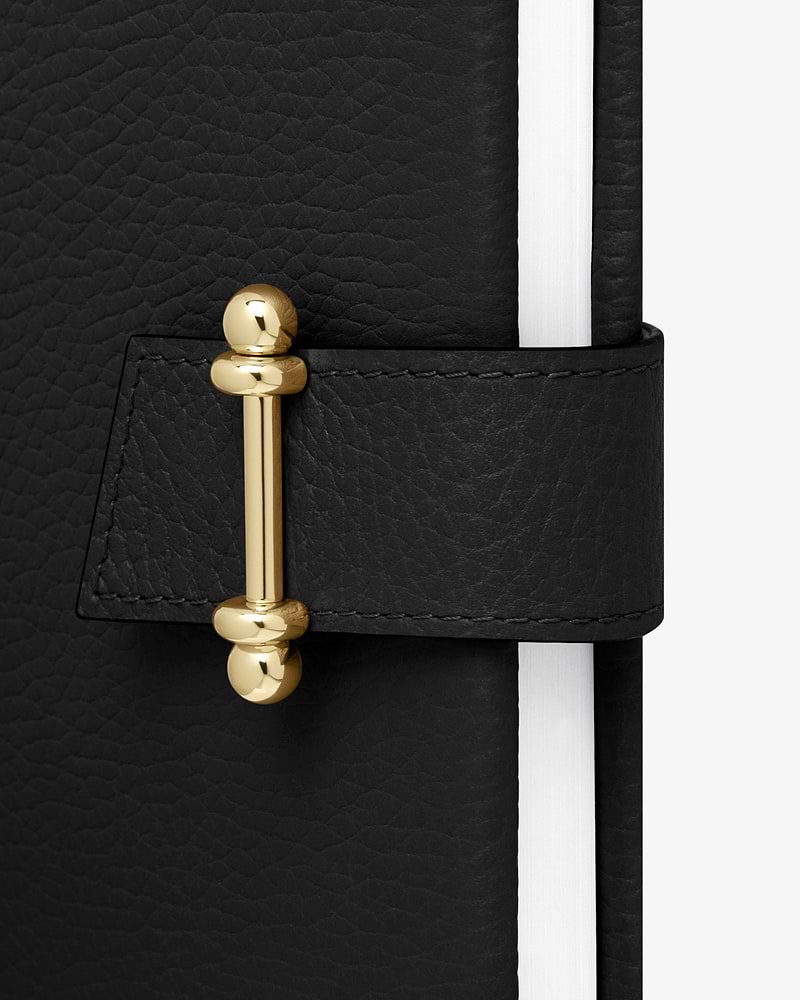 Black leather notebook with gold bar clasp and white page edges.
