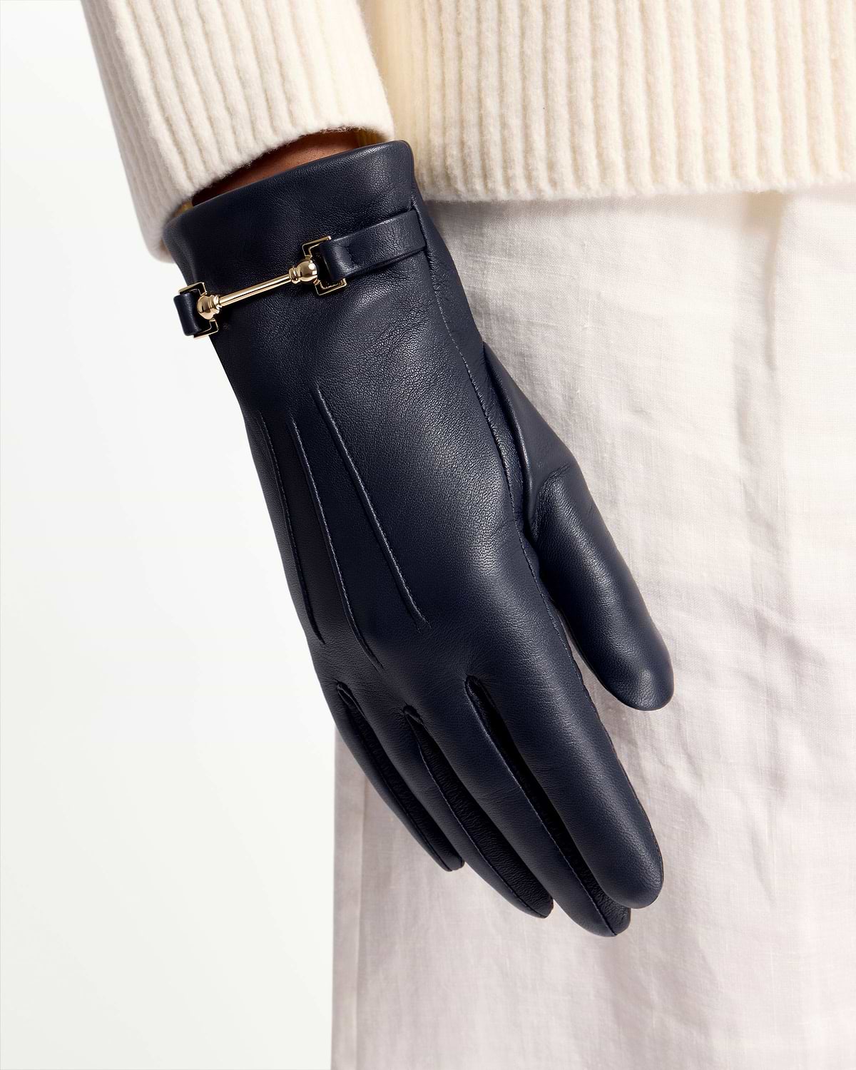 Navy leather glove with gold bar detail worn against cream sleeve and skirt