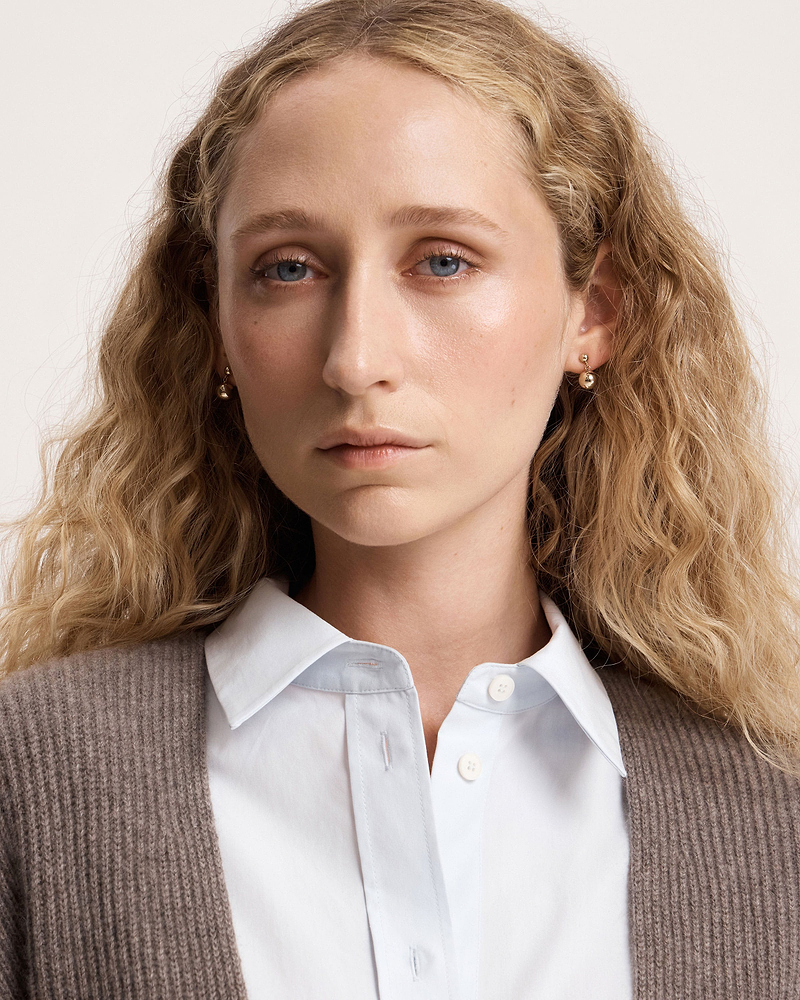 Woman wearing 22 carat gold gilded drop earrings with blue eyes and wavy hair.
