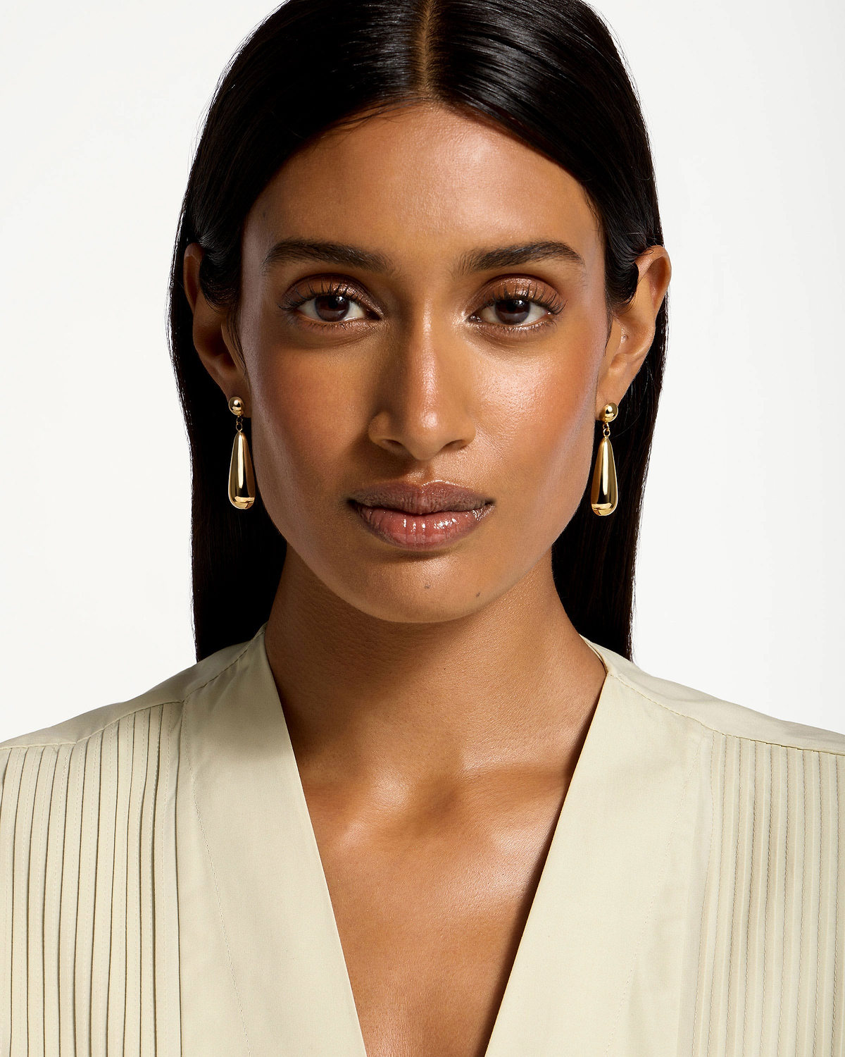 Woman wearing 24 carat gold gilded teardrop earrings, head and shoulders visible.