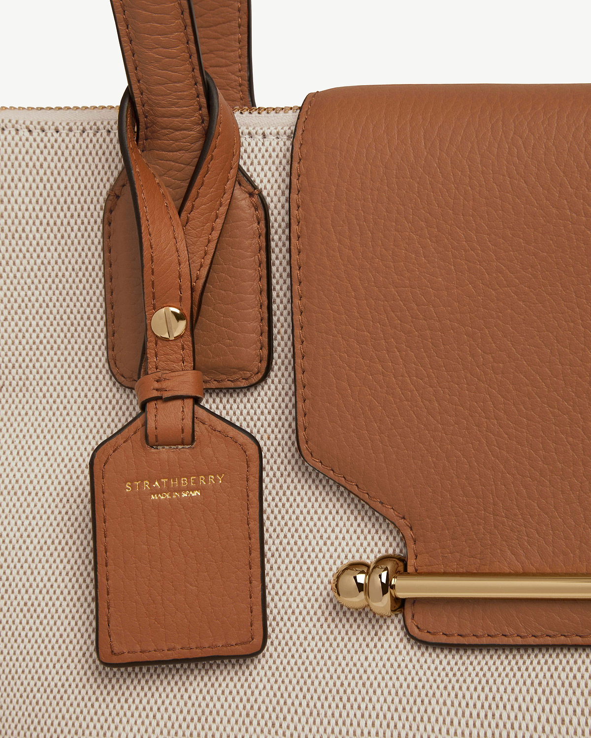 Strathberry tan leather tag attached to cream woven bag with gold hardware.