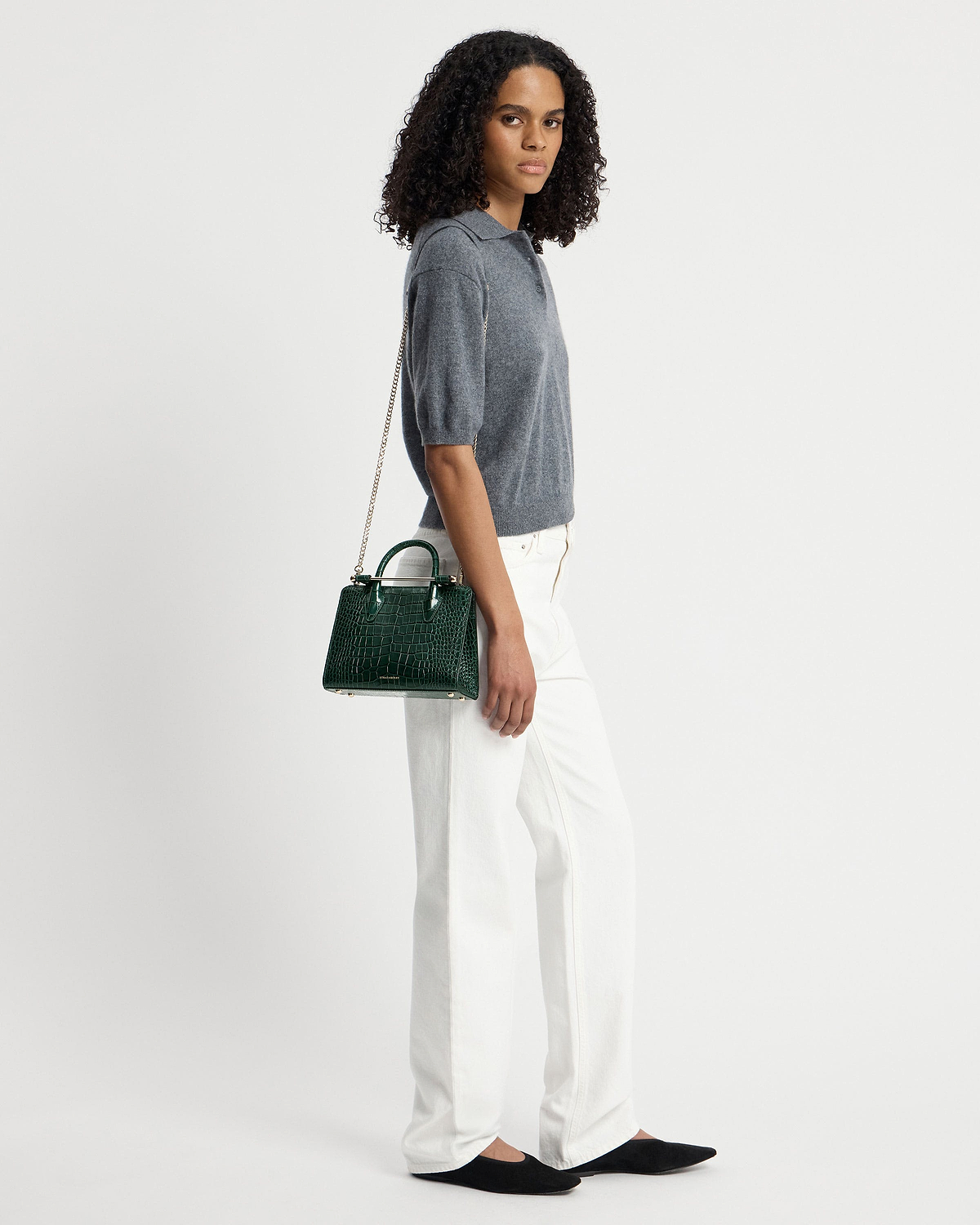 Model carrying green croc mini tote with chain strap at her side.