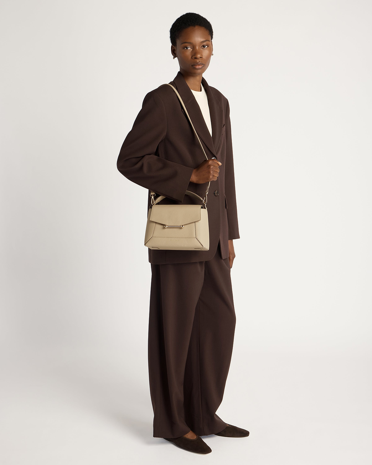 Model wearing a brown blazer holding a sand mosaic bag by shoulder strap.