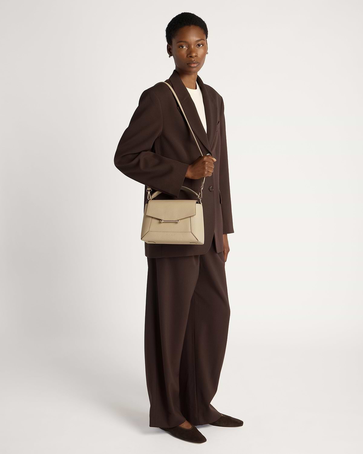 Model wearing a brown blazer holding a sand mosaic bag by shoulder strap.