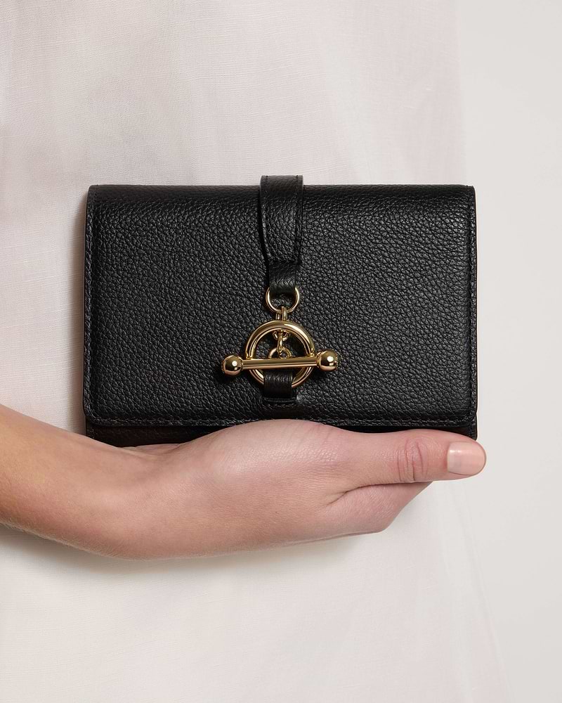 Black leather trifold wallet with gold turn-lock, held in one hand.