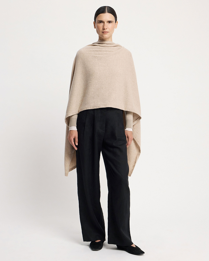 Model wearing an oat cashmere travel wrap draped over shoulders and black trousers