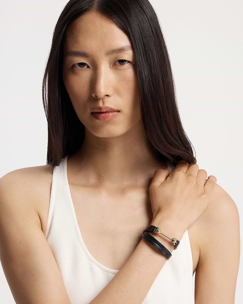 Model wearing a black double-wrap leather bracelet with gold bar and beads.