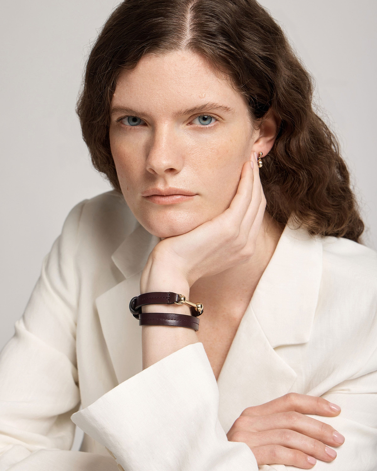 Model's wrist wearing burgundy double-wrap leather bracelet with gold hardware.
