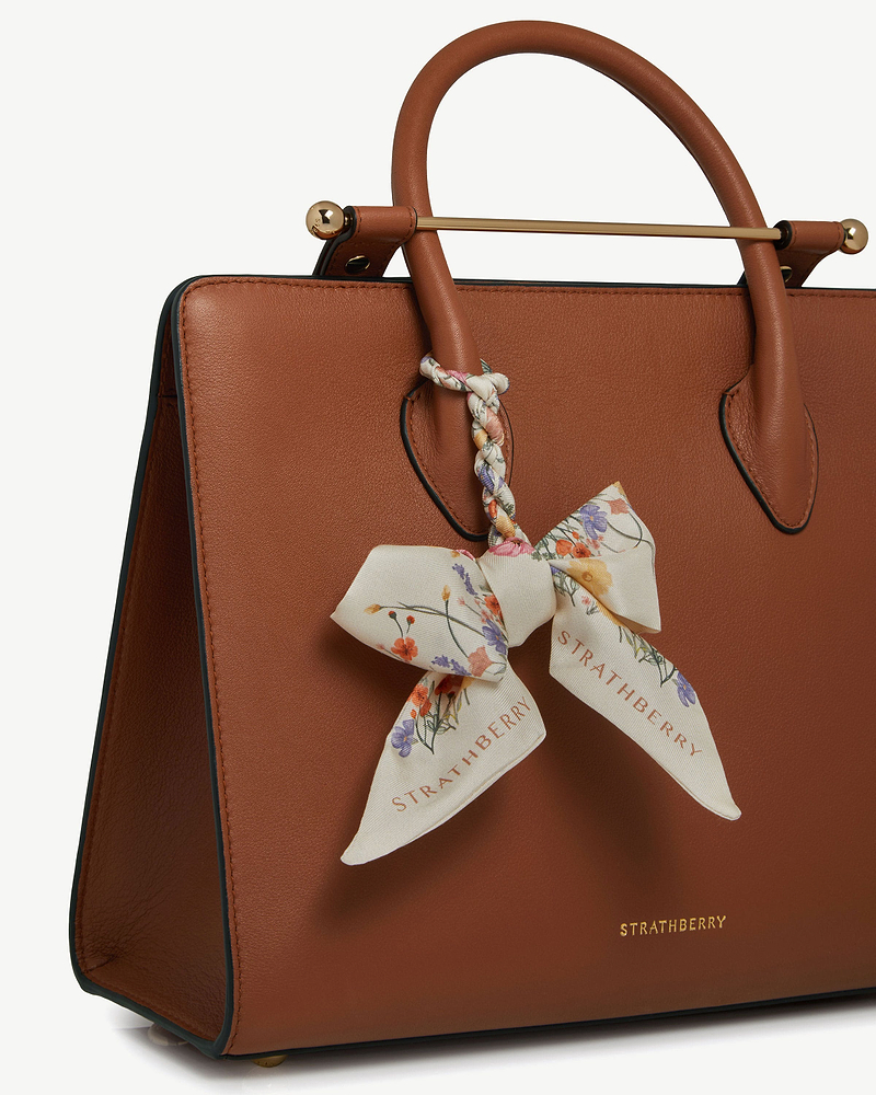 Brown leather handbag with vanilla floral silk skinny scarf tied to handle, Strathberry