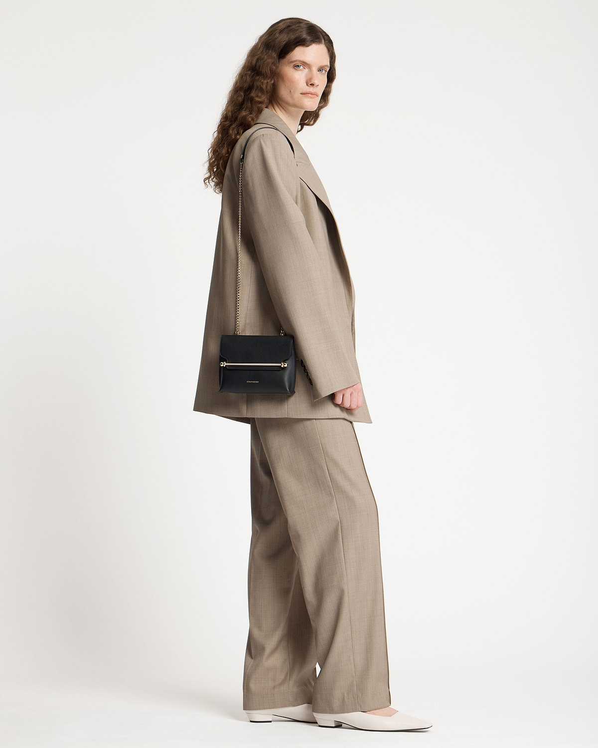 Model wearing a beige suit with a black Strathberry Stylist Mini shoulder bag.