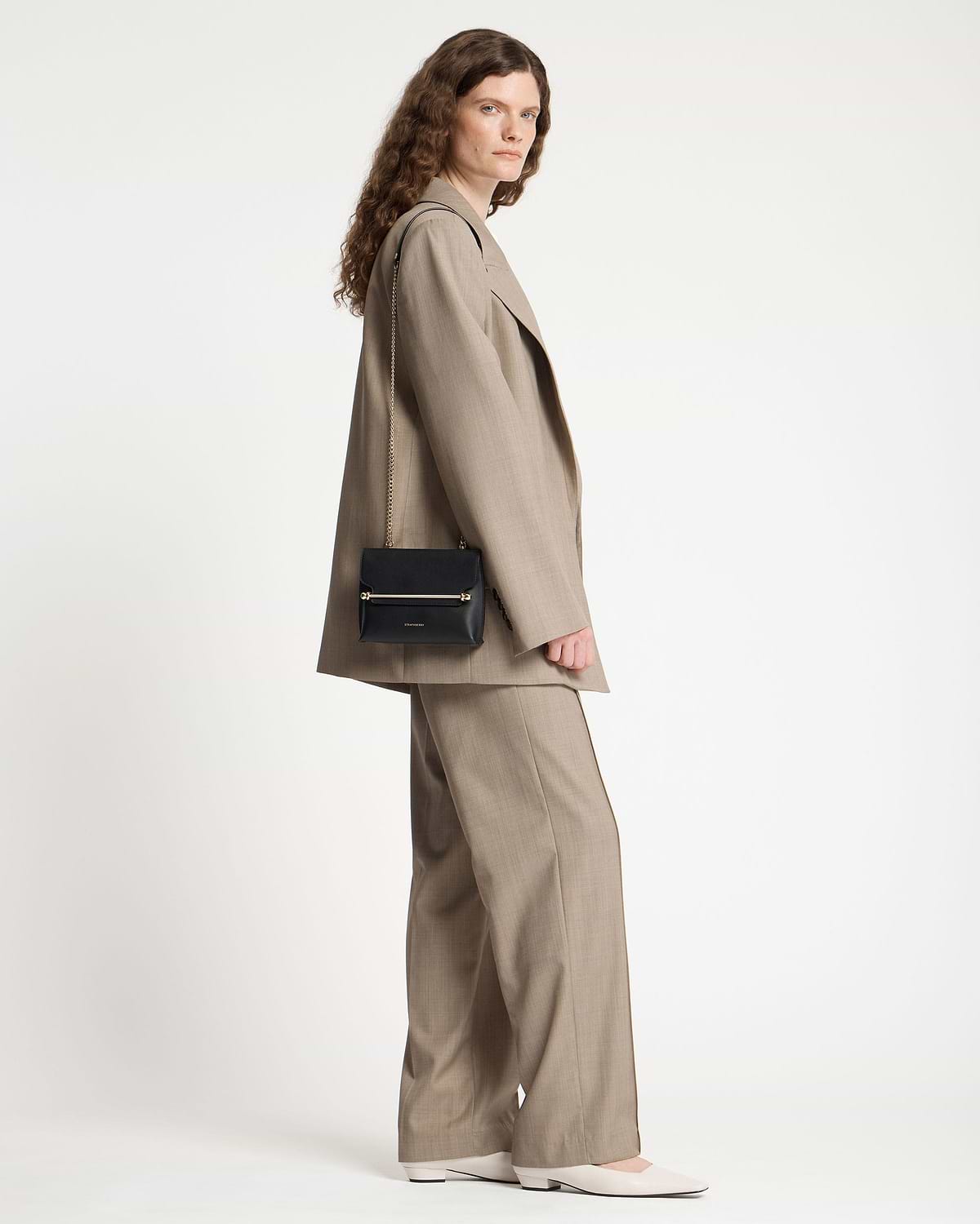 Model wearing a beige suit with a black Strathberry Stylist Mini shoulder bag.